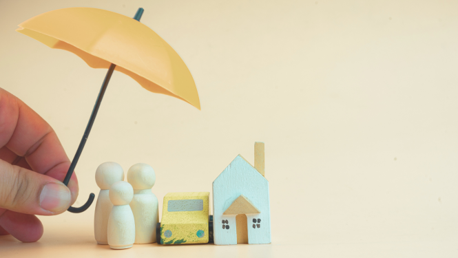 Roka tur dzeltenu lietussargu virs koka figūriņām, mājas un automašīnas simboliem – apdrošināšanas aizsardzības koncepts ģimenei, mājoklim un transportam.