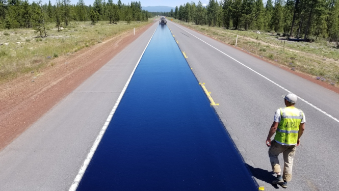 Cilvēks iet gar tikko uzklātu asfalta joslu 